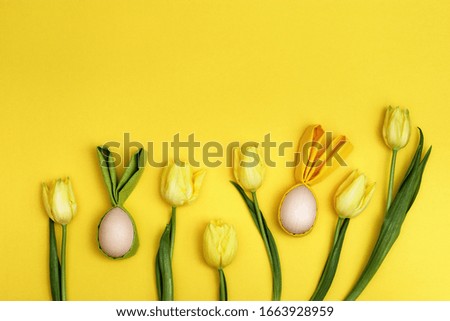 Easter background with decorative wooden eggs us fun easter bunny and bright yellow natural tullits flower. Holiday Flat lay composition.