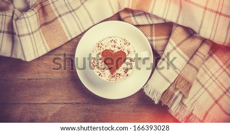 Cup with coffee and shape of the cacao heart on it and scarf. Photo with vintage vignetting.