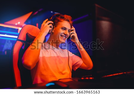 Streamer young man rejoices in victory professional gamer playing online games computer with headphones, neon color.