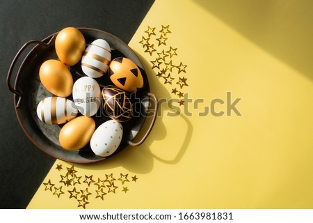 Gold, black, white easter eggs and confetti in the shape of stars on a yellow-black background. Geometry. Minimal concept. View from above. Card with copy space for text. Royalty-Free Stock Photo #1663981831