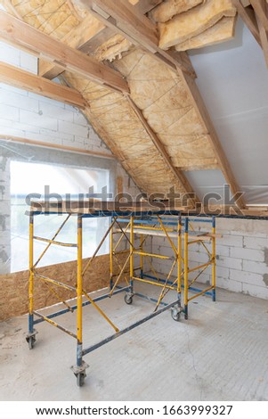 Vertical photo of new house under construction with scaffolding in empty attic room, rockwool insulation material on ceiling and wall