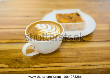 Latte coffee in a white cup on wooden table, hot latte art in flower pattern in a cup at restaurant table, coffee drink for afternoon refreshment after the meeting, food and beverage concept picture
