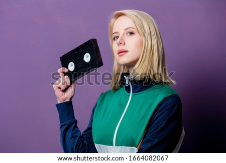 Style blonde woman in 80s clothes with VHS on purple background