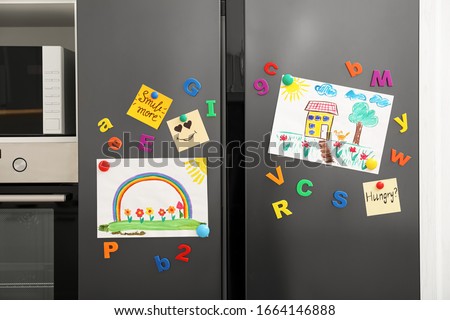 Modern refrigerator with child's drawings, notes and magnets in kitchen