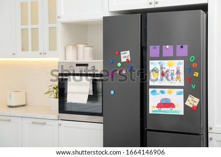 Modern refrigerator with child's drawings, notes and magnets in kitchen. Space for text
