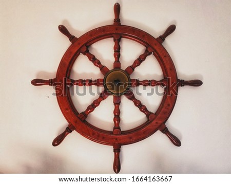 A closeup of a nicely-carved and manufactured wooden steering wheel of ship, mounted on a white wall inside the house. 