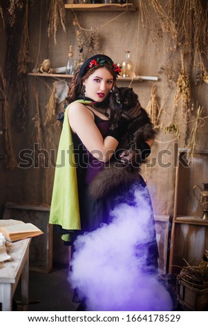A young, attractive witch with a black cat in her hands is cooking a potion in a large black cauldron emitting magical purple smoke.