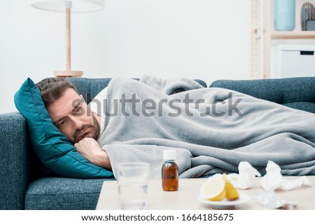 Man wrapped in plaid lying on the sofa feeling sick illness at home Royalty-Free Stock Photo #1664185675