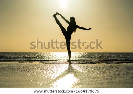 Silhouette of woman standing at yoga pose on the tropical beach during sunset. Caucasian girl practicing yoga near sea water