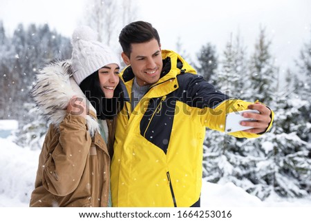 Happy couple taking selfie near snowy forest. Winter vacation