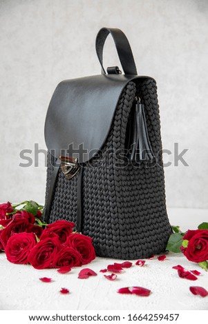 Knitted from synthetic cord black backpack and scarlet roses on a light background. Handmade, creative, copy space