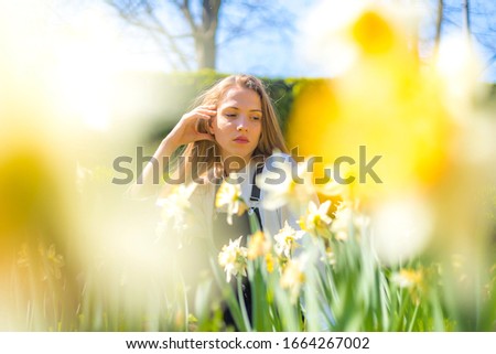 Lifestyle, a caucasian blonde with white shirt behind yellow spring flowers