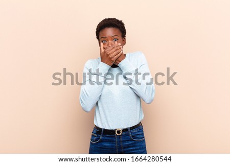 young pretty black womancovering mouth with hands with a shocked, surprised expression, keeping a secret or saying oops