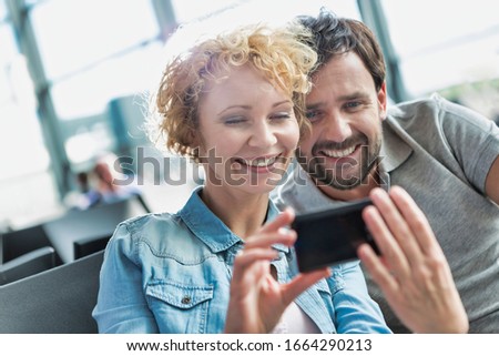Portrait of mature couple taking and looking at their selfie while waiting for boarding in airport