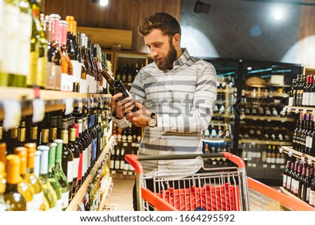 Handsome man at a wine store reading the label on bottle