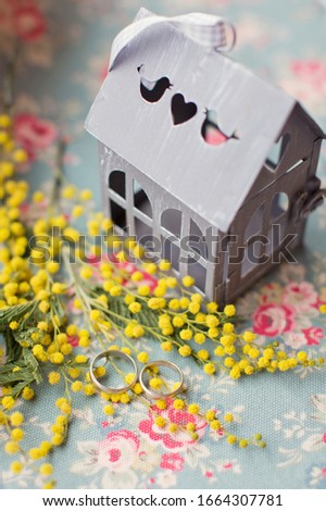 Platinum or silver wedding rings on the metal house with heart and near fresh yellow mimosa flowers