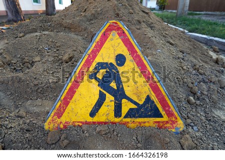 Road work sign placed on a pile of dug up land in the middle of a road being repaired