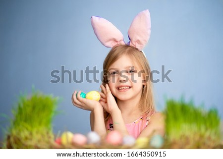 Cute little baby wears bunny ears on Easter day. Cute little girl with easter eggs and green grass. blue background
