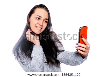 Portrait of a young brunette on a white background taking a selfie on a smartphone. Young woman with a phone.