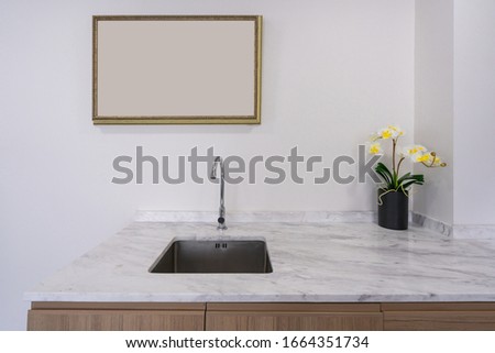 Modern faucet and wash basin sink on white marble counter with wooden photo frame space for advertising, yellow orchid flower in black ceramic vase interior kitchen decoration 