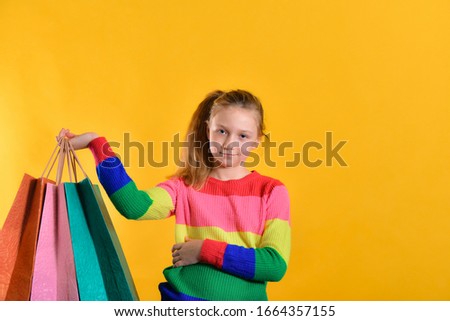 Joyful girl in a colored sweater holds shopping bags in her hand, on a yellow background.