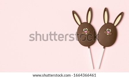 Easter bunny, chocolate sweet candy on stick, cute sweet dessert, top view. Pastel pink background table, Easter symbol egg lollipop character with space for text. Chocolate rabbit candy isolated.