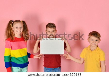 Two boys and a girl are holding a blank poster for inscription and text.