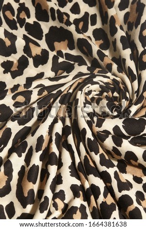 Macro shot of a beige fabric with black and brown leopard print. The cloth folds are lined as a flower-form figure.  