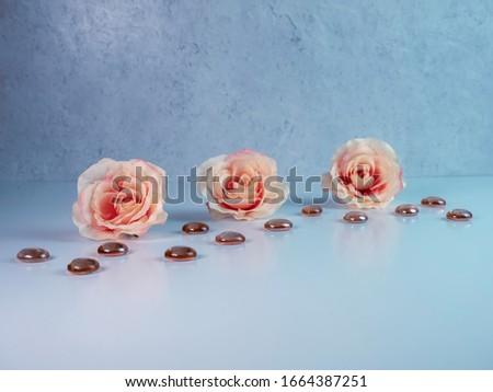 3 peach colored roses lined up with dark orange brown glass flat marbles on a white surface with a plaster background.  Soft and elegant with the reflection against the white surface.