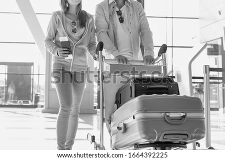 Black and white photo of man pushing baggage cart for check in with her daughter at airport