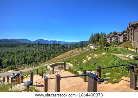 Beautiful open valley with Cascade mountains and pine trees and large lodge with staircase and fire pit.