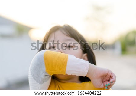 Coronavirus Covid-19 virus and Air pollution pm2.5 concept.Spreader Asian child girl sneezing on hinge joints arm outdoor for protect from virus stop corona virus covid19 outbreak.Sick child kid. Royalty-Free Stock Photo #1664404222