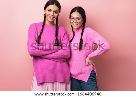 Image of two happy teenage girls with braids in casual clothes smiling at camera isolated over pink background