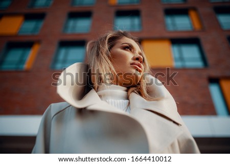 Gorgeous cheerful blonde girl looking away while strolling at spring street.Successful female person enjoying leisure time outdoors during city walk