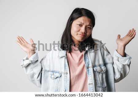 Portrait of an annoyed young asian woman wearing denim jacket looking at camera isolated over white background