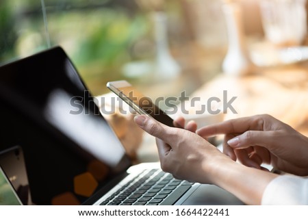 Woman hand holding white mobile phone on a table with a laptop in office. Royalty-Free Stock Photo #1664422441