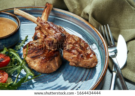 A grilled rack of young calf or lamb (beef) with peanut sauce and cherry tomatoes in a blue plate on a wooden background. Selective focus, close up
