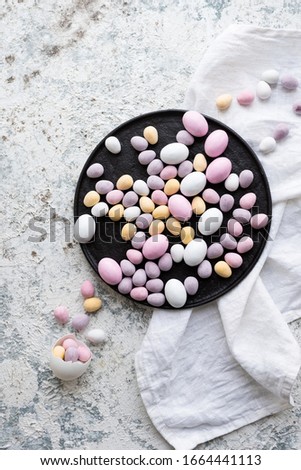 Easter composition with mini chocolate eggs in pastel colors on grey concrete background. Happy Easter Holidays. Top view. Copy space.