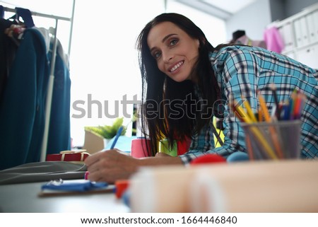 Woman smiles while modeling new custom clothes. Girl smiles and drawers design clothes she wants to sew during training course. Atelier worker makes notes on order to complete job accurately