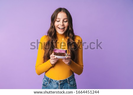 Image of young beautiful woman with long brown hair smiling and holding birthday cake isolated over violet background