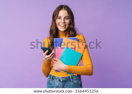 Image of young beautiful student girl wearing eyeglasses holding exercise books and cellphone isolated over violet backgroun\