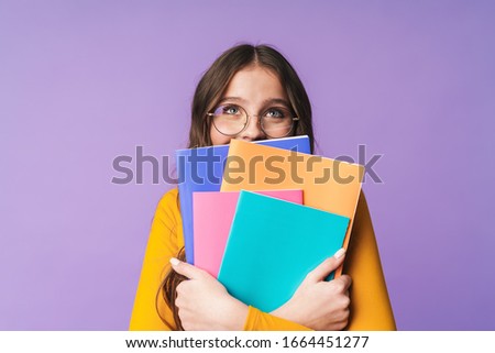 Image of young beautiful student girl wearing eyeglasses holding exercise books isolated over violet background