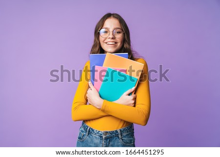 Image of young beautiful student girl wearing eyeglasses smiling and holding exercise books isolated over violet background