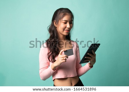 Young Asian woman is shopping online with credit card and tablet on cyan background