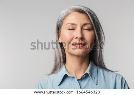 Image of adult mature woman with long white hair wearing shirt standing with eyes closed isolated over gray background Royalty-Free Stock Photo #1664546323