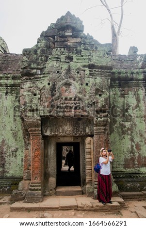 Young female tourist with camera taking picture of the  entrance to ancient Preah Khan temple in Angkor. Siem Reap, Cambodia.