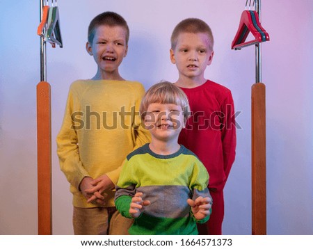 Cute blond boys in red, yellow and green sweaters at home. teenagers climbed into locker room and play among empty hangers