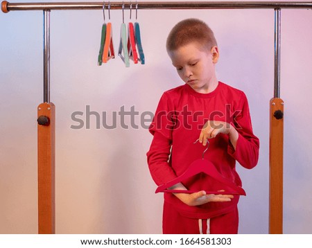 Cute blond boy in red sweater at home. teenager climbed into locker room and plays among among empty hangers