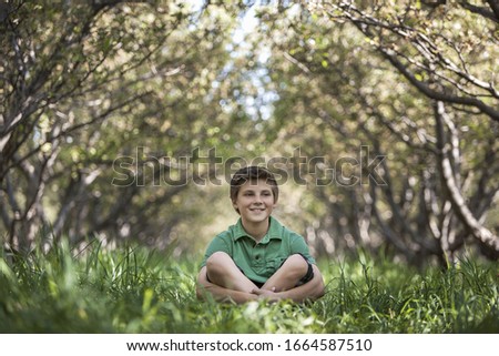 A boy sitting crosslegged in a woodland tunnel with tree branches meeting overhead.