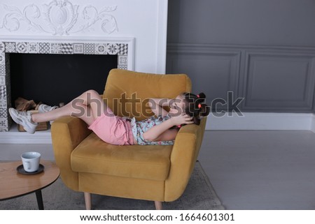 portrait of a young funny girl of seven years old with a funny hairstyle sitting in a large comfortable chair in a good mood and grimaces